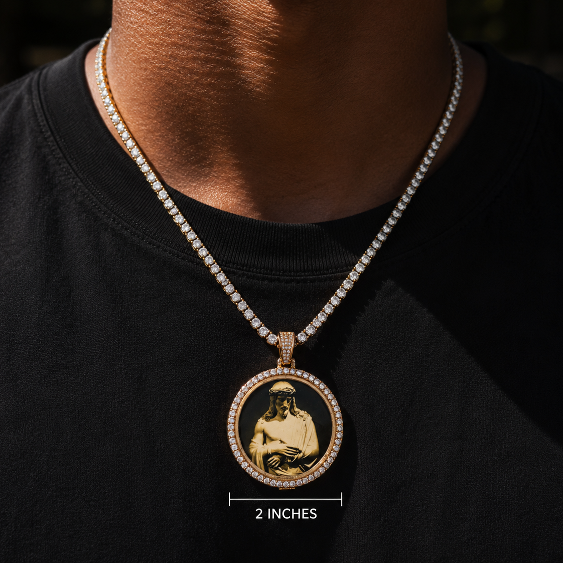 A close-up of a person wearing a gold-tone pendant necklace with a detailed portrait medallion, set against a black t-shirt. A white text overlay at the bottom indicates the size is 2 inches.